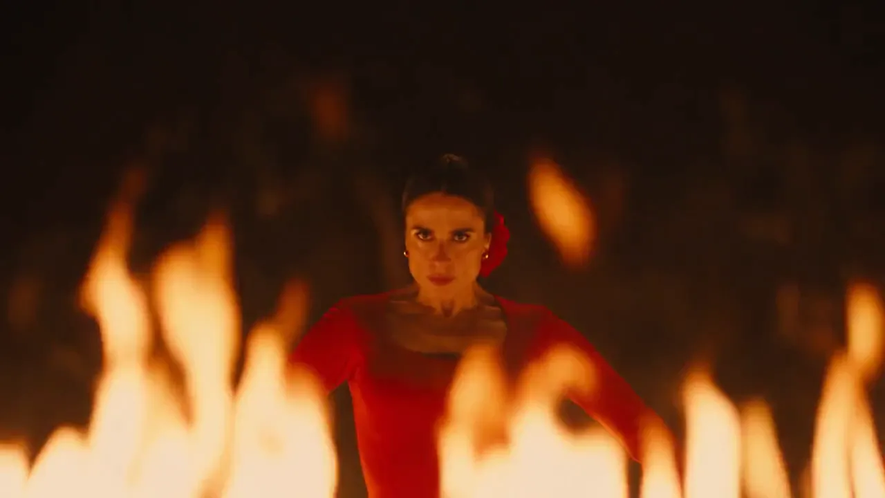 A flamenco dancer in a red dress performs inside a ring of fire.